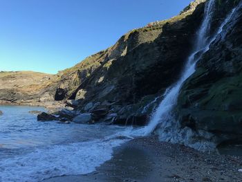 Scenic view of waterfall against clear sky at merlin's cave, tintagel