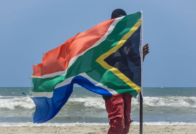 Flag standing on beach against sky
