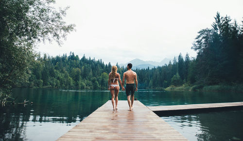 Rear view of people standing on pier over lake against sky