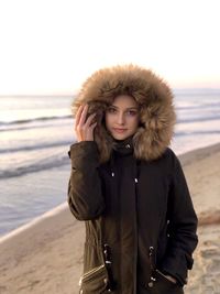 Portrait of young woman standing at beach during winter