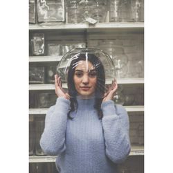 Portrait of young woman head in glass container against shelf