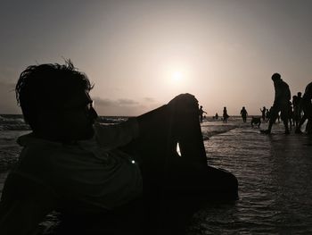 Silhouette man sitting on beach against clear sky during sunset