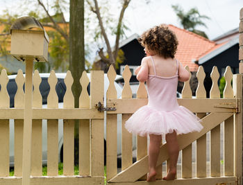 Rear view of girl standing by fence at yard