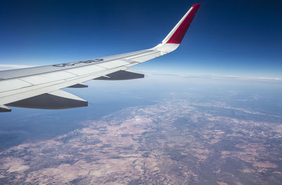 Aerial view of airplane wing over landscape against blue sky