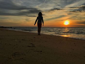 Silhouette woman standing on beach against sky during sunset