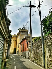 Electricity pylon on road against cloudy sky