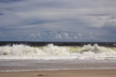 Sea waves splashing at beach against sky