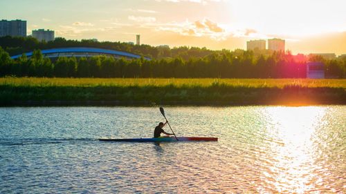 Man rowing on river against sky at sunset