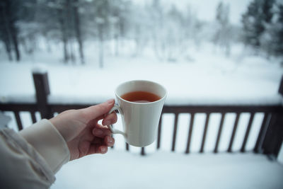 Cropped hand of woman holding cup against snow