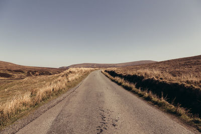 Road amidst field against clear sky