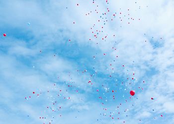 Low angle view of multi colored balloons flying against sky