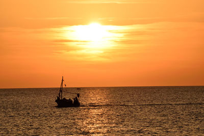 Silhouette sailboat in sea against orange sky