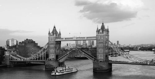 Bridge over river in city against cloudy sky