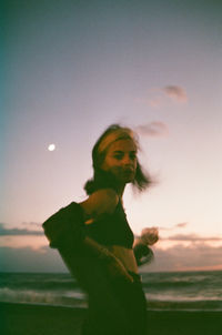 Portrait of young woman standing at beach during sunset