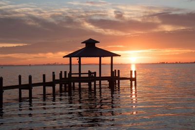 Silhouette wooden posts on beach against sky during sunset