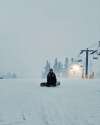 Man sitting on snow covered land against sky