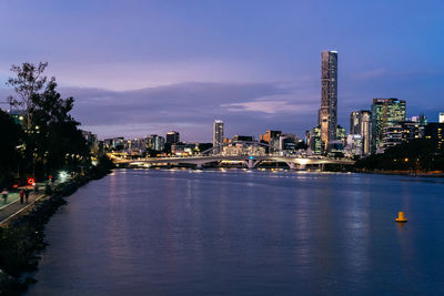 Illuminated city by sea against sky at dusk