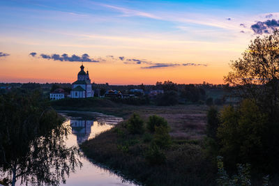 Scenic view of river by buildings against sky during sunset