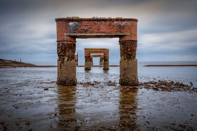 Rusty metallic structure on beach against sky