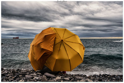 Digital composite image of yellow umbrella on beach against sky