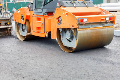 The metal cylinders of the large vibratory roller roll on the new road surface .