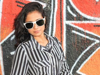 Portrait of beautiful woman wearing sunglasses against graffiti