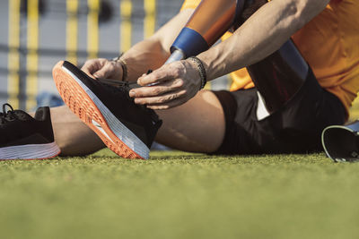 Hands of athlete tying shoelace of prosthetic leg sitting on grass