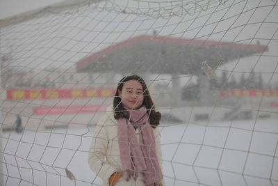 Portrait of woman looking through fence during winter