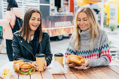 Two satisfied happy hungry women eat burgers in the street market.