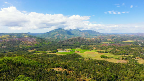 Fertile farmlands with growing crops and mountains with clouds against a blue sky. 