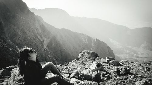 Woman sitting on mountain against sky