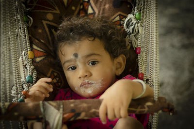 A north indian baby child eating curd at home with his face on black dots