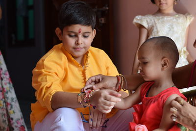 Boy wearing rakhis while sitting with toddler sister at home