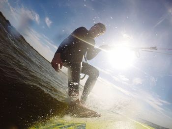 Low angle view of man kiteboarding on sea against bright sun