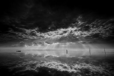 Silhouette man standing on shore against sky