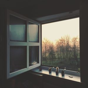 Bare trees on field seen through window at sunset