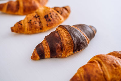 Close up of bunch of delicious brown and chocolate croissants laid out on a white table	
