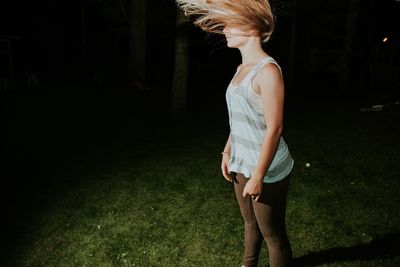 Young woman with tousled hair while standing on grassy field at night