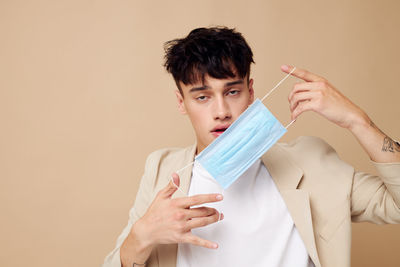 Portrait of young man holding mask against beige background