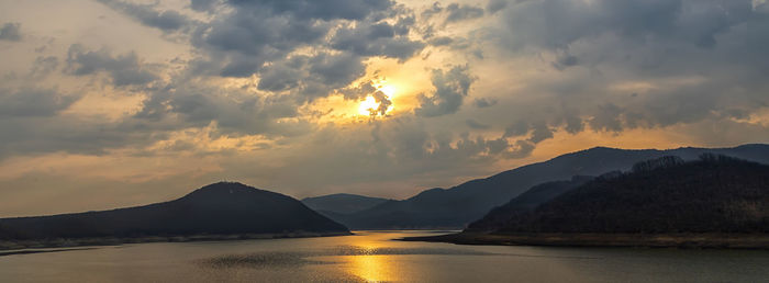 Panoramic view of a lake among hills and mountains with sun reflection