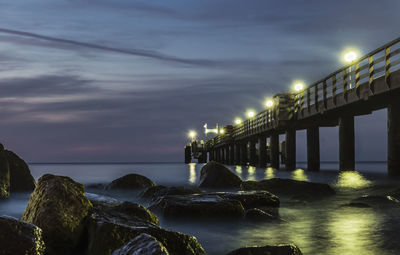 Illuminated bridge over sea against sky at night