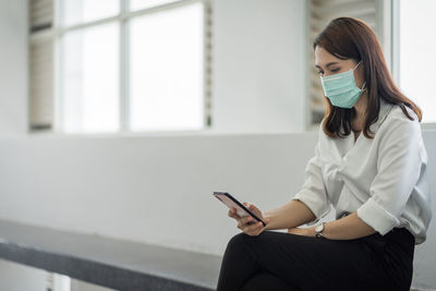 Woman using mobile phone while sitting on laptop