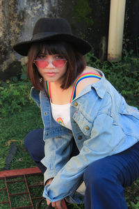 Portrait of young woman wearing sunglasses and hat crouching outdoors