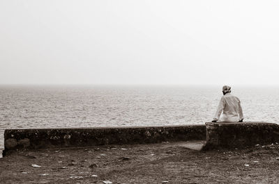 Rear view of man standing at beach against clear sky