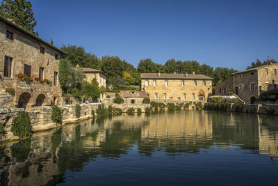 Buildings by river against clear blue sky