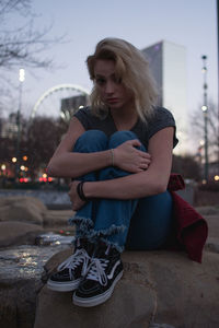 Young woman sitting at park in city against sky