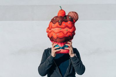 Midsection of man holding artificial ice cream against white wall