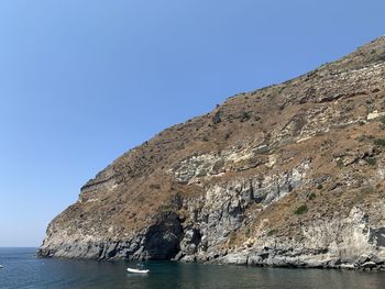 Rock formations by sea against clear blue sky