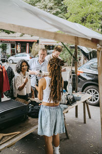 Rear view of female owner communicating with customers while standing near stall at flea market