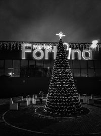 Illuminated christmas tree against building at night